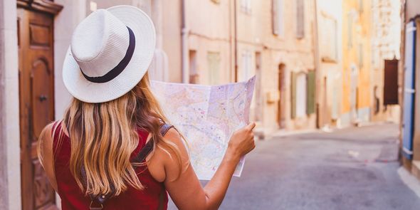 Femme en vacances, dos à l'appareil photo, penchée sur une carte dans une rue calme et ensoleillée.