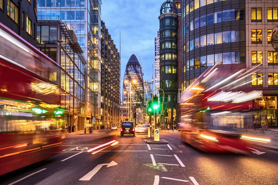 Photo nocturne du Gherkin de Londres prise avec une vitesse d'obturation lente, avec deux bus londoniens au premier plan.