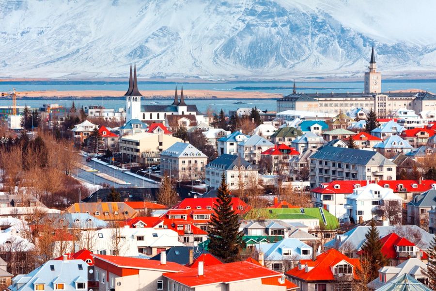 Photo des toits éclatants de Reykjavik, avec la mer en arrière-plan et une montagne enneigée au loin.