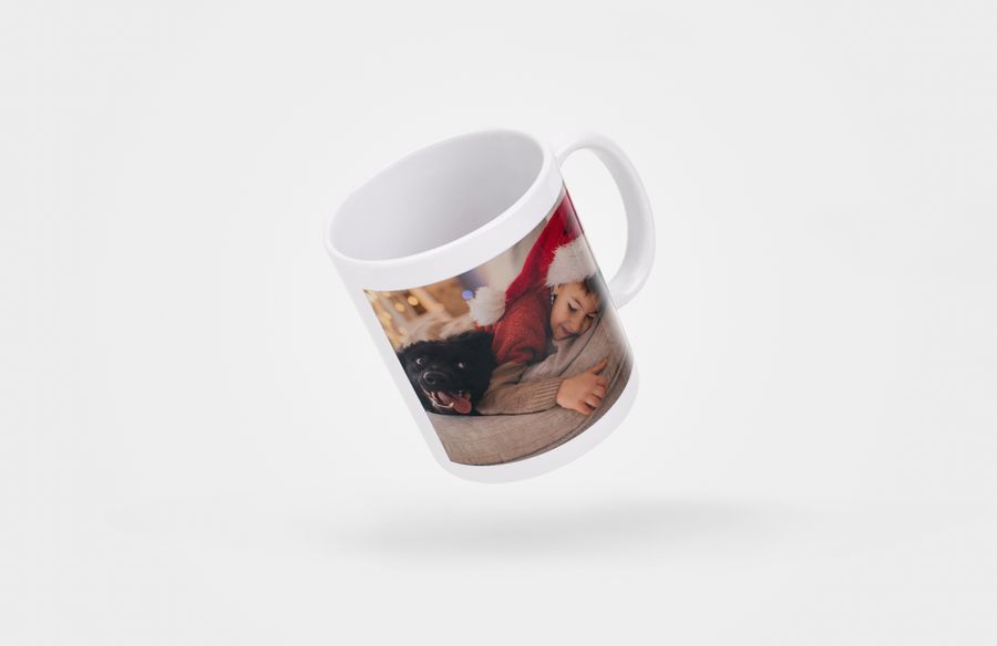 Une tasse photo avec l'image d'un petit garçon portant un chapeau de Père Noël allongé sur le canapé avec son chien.