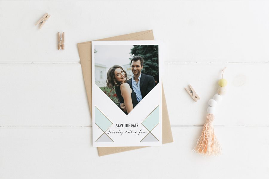 Une carte de mariage personnalisée Save-the-date avec photo devant un fond blanc avec des petites pinces à linge en bois de chaque côté.